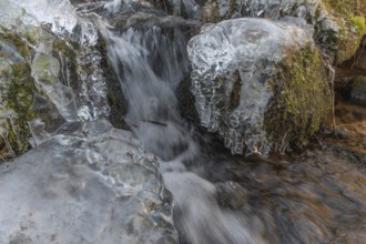 Branches are covered with ice near the river. The water flows gently and forms ice formations on