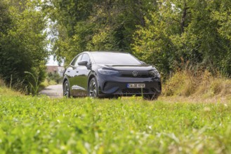 Black car on a country road surrounded by greenery in cloudy sky, VW ID5 electric car, Deer