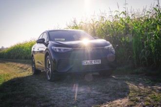Black car on a dirt road next to a corn field with bright sunlight on the hood, VW ID5 electric