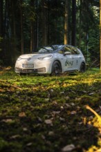 Car during the day in the forest on mossy ground, sunlight falling on the scene, VW ID3 electric