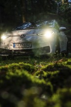 Car with headlights switched on in dark forest on mossy ground, VW ID3 electric car, Deer