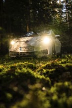 Car in the dark forest, headlights glow on mossy ground, mystical atmosphere, VW ID3 electric car,