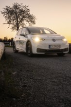 Car driving along a street with glowing headlights in the evening, VW ID3 electric car, Deer