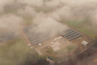Fog-covered construction site with solar systems, several vehicles visible, energy revolution,