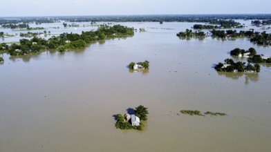 An aerial view shows widespread flooding submerging villages and farmland, with isolated homes and
