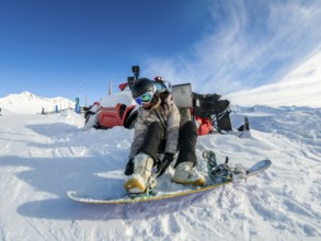 Young woman strapping her snowboard boots into the bindings on a snowy slope under a clear blue