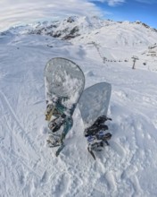 Snowboards rest in deep snow on a high mountain summit, offering a panoramic view of an expansive