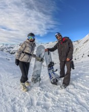 Couple standing with snowboards on a snowy mountain slope, smiling under a blue sky while enjoying
