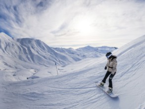Female snowboarder in helmet and goggles carving fresh snow on a sunny alpine slope, panoramic