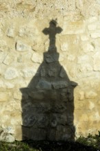Mazerier village. A shadow of a stone cross appears on an old, weathered stone wall. Sunlight