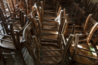 Many old wooden chairs are stacked in disarray, upside down in a church. France. Europe