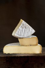 Three pieces of Saint-Nectaire cheese are stacked on top of each other, set on a dark wooden