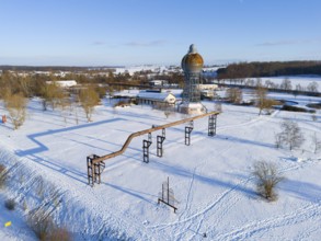 Snowy industrial structure with a large tower in an open landscape under clear sky, aerial view,