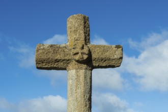 Stone cross stands tall against a bright blue sky with scattered white clouds in the background,