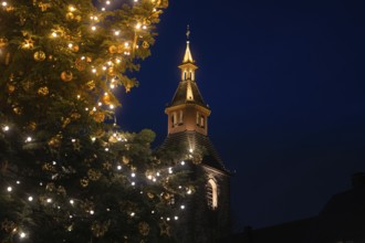 Glowing church tower next to a festively decorated Christmas tree at night, Nagold, Calw district,