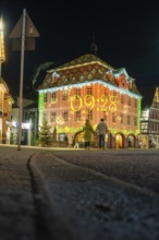 A family looks at a historic building decorated with glowing projections at night, Nagold, Calw