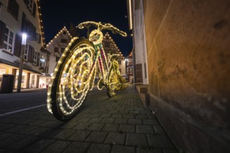 A bicycle artfully decorated with lights stands at night in the illuminated old town, Nagold, Calw