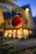 Red Christmas ball on pine branch, evening mood with blurred lights in the background, Nagold, Calw