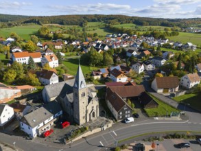 A village with church surrounded by hills and green meadows in autumn, aerial view, Niederkalbach,