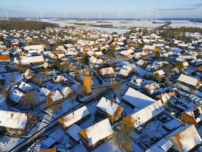 Snowy village with a central water tower surrounded by wind turbines and snow-covered houses under