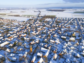 Aerial view of a snowy village with wind turbines on the horizon and a water tower in the center,
