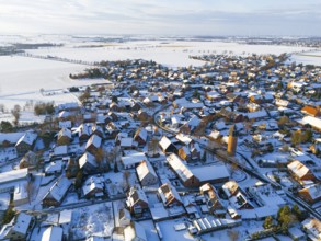 Bird's-eye view of village, with snow-covered roofs, a water tower and vast, snow-covered fields,