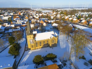 Snowy church in a village with a rural atmosphere, surrounded by wind turbines in a quiet winter