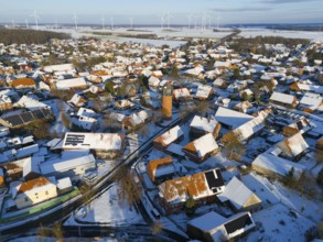Snowy village with a water tower and a variety of wind turbines in the distance under a clear sky,