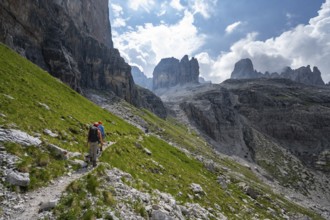 Two mountaineers on a hiking trail in front of a picturesque mountain landscape with rocky peaks,