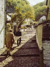 Men carrying wooden sled or sledge used for transport on steep hill of cobbled main village street,