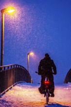 Winter weather, blowing snow, person with e-bike, bicycle on snowy bridge, footpath bridge, steep