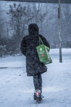 Winter weather, blowing snow, woman with e-scooter on snowy road, North Rhine-Westphalia, Germany