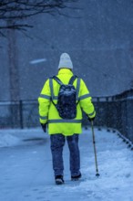Winter weather, blowing snow, man walking on a snowy sidewalk with a walking stick, North