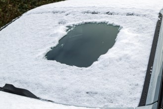 Snow-covered car window with scratched peephole area, typical winter scene