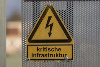 (Photo montage) Text CRITICAL INFRASTRUCTURE on a warning sign for a high-voltage line