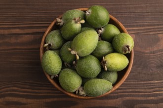 Ripe Feijoa in wooden bowl on brown wooden background, top view, flat lay, close up, minimalism
