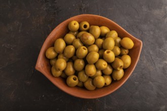 Fresh green olives in ceramic clay bowl on black concrete background. Top view, flat lay, close up