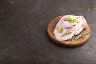 Raw Turkey Thigh with spices and rosemary on cutting board on black concrete background. side view,