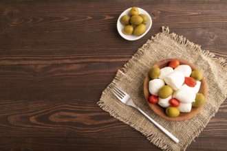 White Mozzarella cheese, with tomatoes and olives in wooden bowl on brown wooden background and