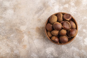 Wooden bowl with raw edible ?hestnuts on brown concrete background, top view, flat lay, copy space,