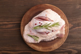 Raw Turkey Thigh with spices and rosemary on cutting board on brown wooden background. top view,