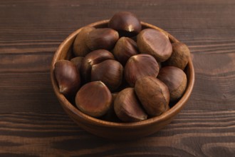 Wooden bowl with raw edible ?hestnuts on brown wooden background, side view, close up, minimalism