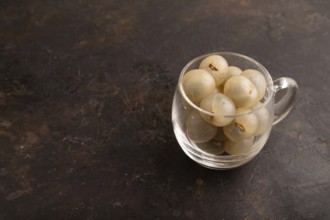 Ripe peeled Longan in glass on black concrete background, side view, copy space, minimalism