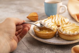 French lemon tart with meringue with hand on brown concrete background, cup of coffee, orange linen