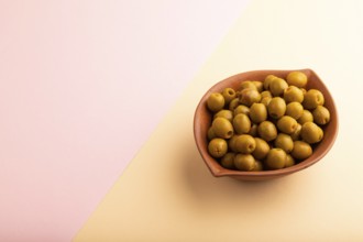 Fresh green olives in ceramic clay bowl on pink and orange pastel paper background. side view, copy