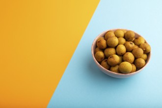 Ripe Longan in ceramic bowl on blue and orange pastel paper background, side view, copy space,