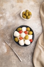 White Mozzarella cheese, with tomatoes and olives in blue bowl on brown concrete background and
