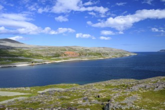 Green meadows on the banks of Syltefjord with clouds in the blue sky, landscape with a lake and