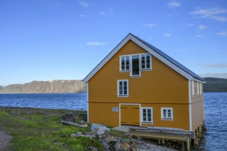 Yellow wooden house on the seashore under blue sky in natural landscape, yellow house overlooking