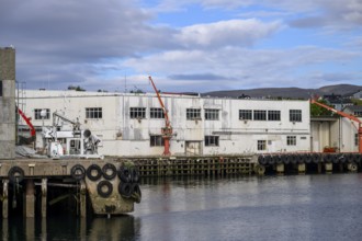 Fishing industry industrial building at the harbour with red loading cranes on the quay, water and